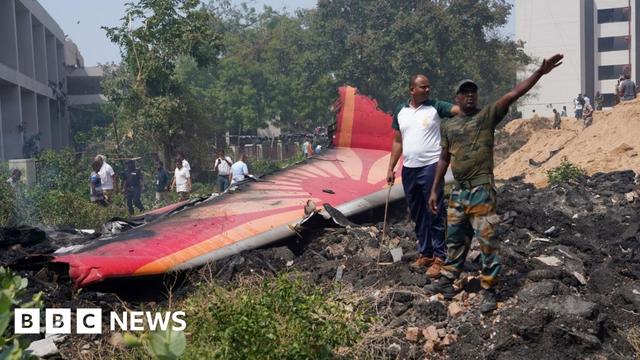 Two rescue workers stand beside part of the fuselage of the Air India plane, bearing the airline's colour scheme at the crash site