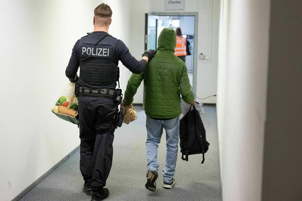 Ein Polizeibeamter bringt einen Mann zu einem Abschiebeflug, wir sehen sie von hinten Ein Polizeibeamter bringt einen Mann zu einem Abschiebeflug, wir sehen sie von hinten