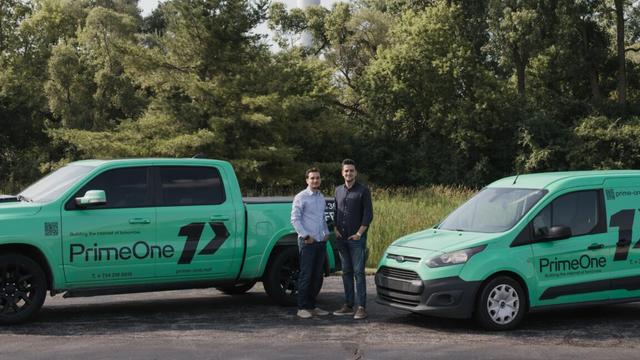 Two young men stand outside next to service vans with a logo for Prime-One, the Internet provider they founded.