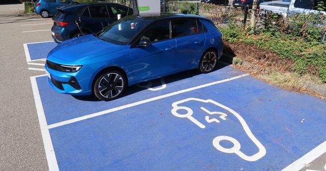 Ein E-Auto tankt Strom. Daneben ist ein freier Parkplatz für E-Autos. Ein E-Auto tankt Strom. Daneben ist ein freier Parkplatz für E-Autos.