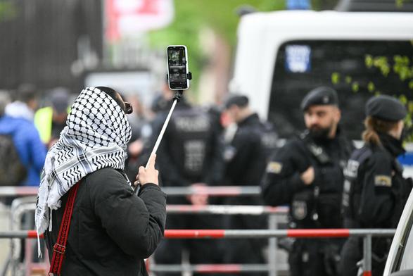 Ein Mensch mit Kufiya filmt Polizisten hinter einer Absperrung