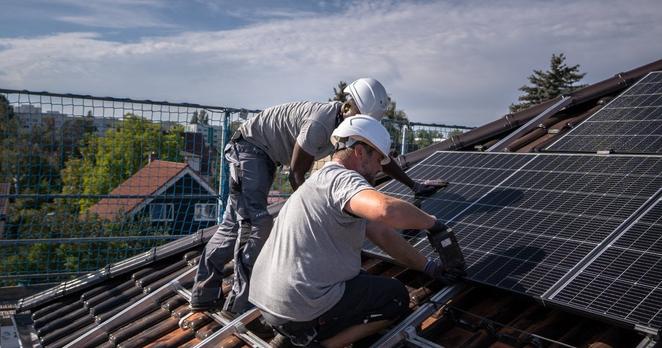Zwei Männer installieren auf einem Hausdach eine Photovoltaik-Anlage Zwei Männer installieren auf einem Hausdach eine Photovoltaik-Anlage