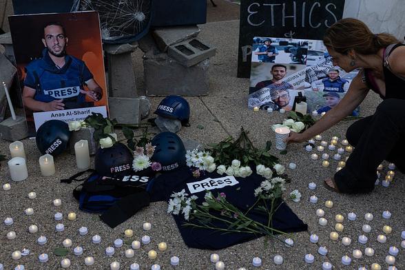 People hold photos, lay flowers and light candles during a vigil honoring journalists killed in Gaza.