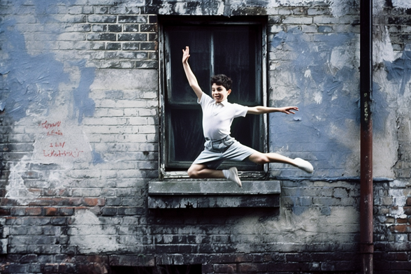 A young boy in an improbably high flying leap in front of the outside of an old building