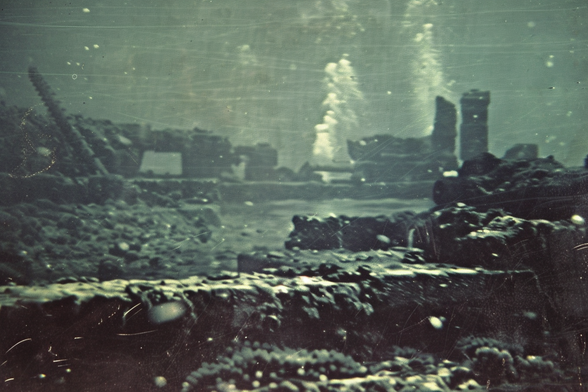 The ruins of an ancient city at the bottom of the ocean, with crumbling towers and toppling columns, and a stream of bubbles possibly indicating habitation