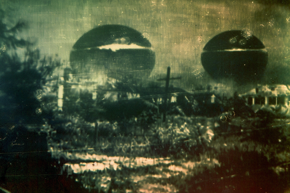 Two very large surveillance spheres hover over houses on the edge of town