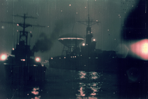 Two warships at night, showing lights. One has a large inverted cone mounted aft of the superstructure