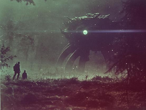Silhouetted figures in a misty forest facing a large creature with glowing light.
