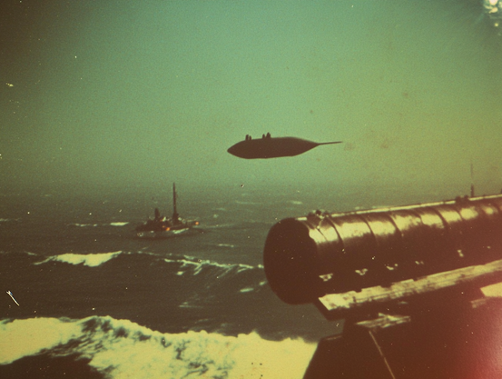Elliptical object in the sky over a rough ocean; a platform on the horizon and metallic structure in foreground.