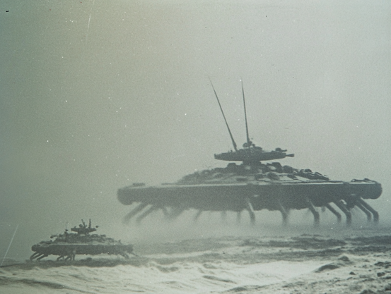 Two large, mechanical spider-like machines in a foggy, barren landscape.