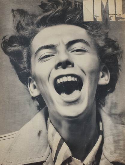 The image is a vintage-style close-up photograph of a person with a joyful expression, laughing heartily. The person has wavy hair blown upwards, suggesting motion or wind. They are wearing a light-coloured jacket and a striped shirt underneath. The image is presented in a monochromatic colour palette, with a grainy texture that gives it an aged appearance. In the upper-right corner, part of a magazine title is visible, partially obscured and cropped.