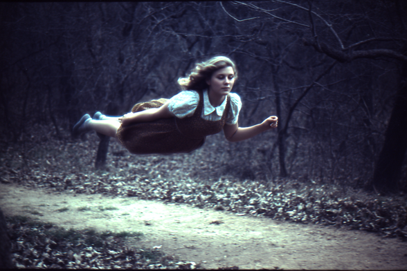 Person appearing to levitate horizontally over a forest path.