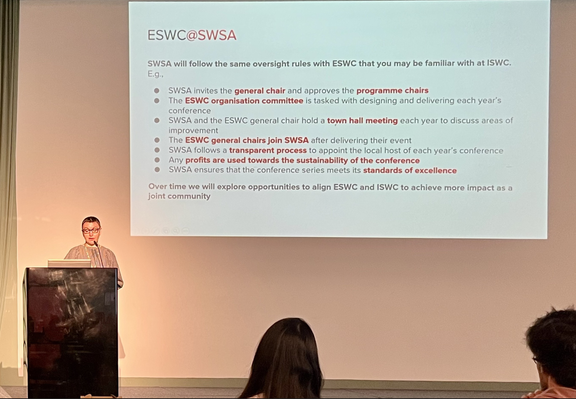 The image shows a presentation slide titled "ESWC[@]SWSA" displayed on a large screen. The slide outlines the oversight rules that SWSA will follow with ESWC, similar to those at ISWC. The text includes bullet points detailing the roles and responsibilities, such as inviting the general chair, approving program chairs, and holding town hall meetings for improvement. It also mentions the transparent process for appointing local hosts, using profits for sustainability, and ensuring the conference…