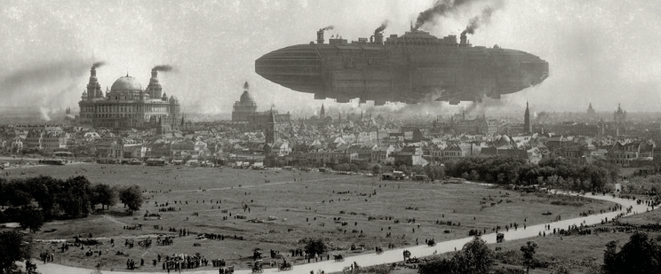 A large airship hovers over a historical cityscape with a prominent domed building and a public park in the foreground.