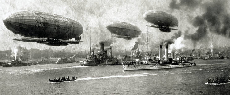 Historical scene of airships above a naval fleet with smoke-filled skies.