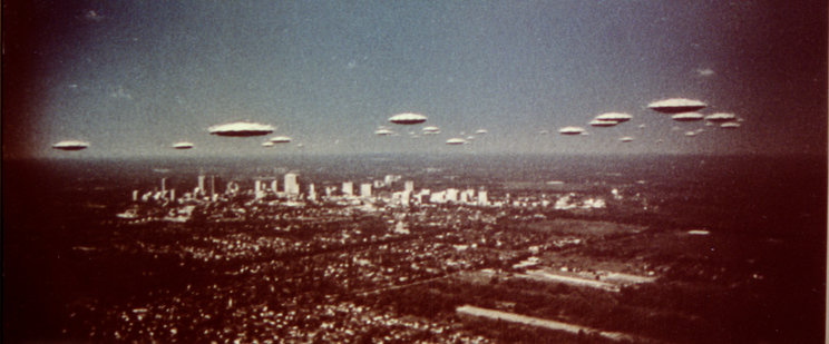 Aerial view of a city skyline with multiple UFOs in the sky above.