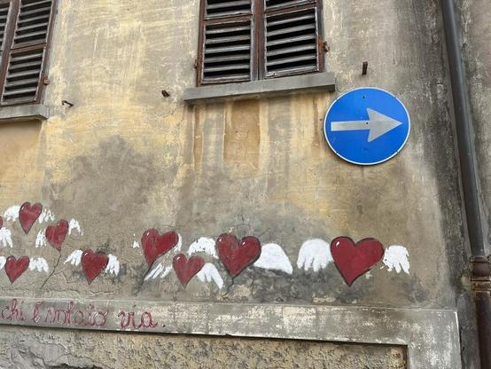 Flying hearts floating down the street, painted on a wall below a blue one way sign.