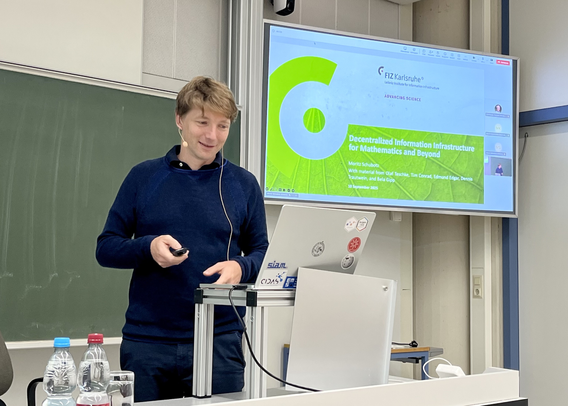 Moritz Schubotz standing in front of the projection of his presentation slides showing the opening slide with the title.