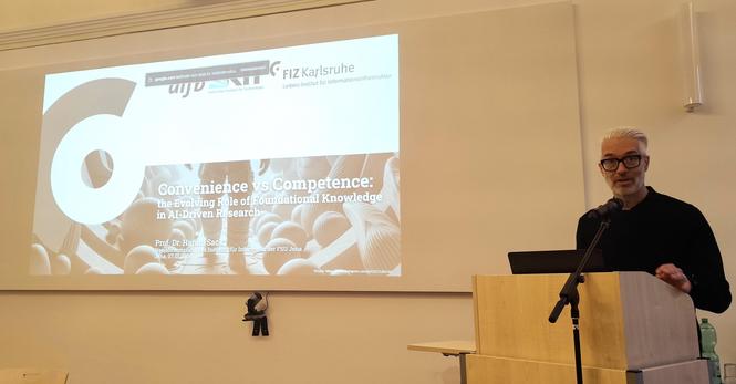 Me standing at the speakers desk, dressed completely black. Left from me, the cover slide of my talk is being projected showing an AI-generated astronaut in an alien spaceship illustrating the title of the talk: Convenience vs Competence... photo by Christian Knüpfer (thanks a lot!)
