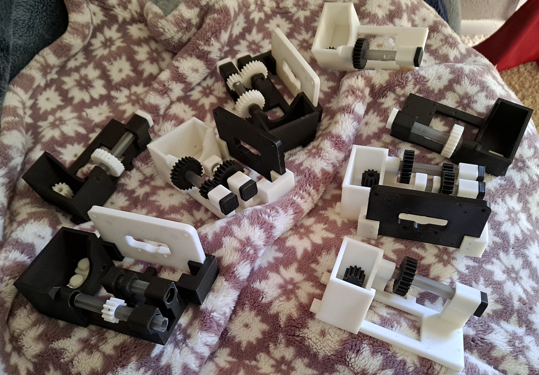 A bunch of black-and-white gearboxes, made from 3d-printed parts and ballpoint pens, scattered on a fuzzy blanket.