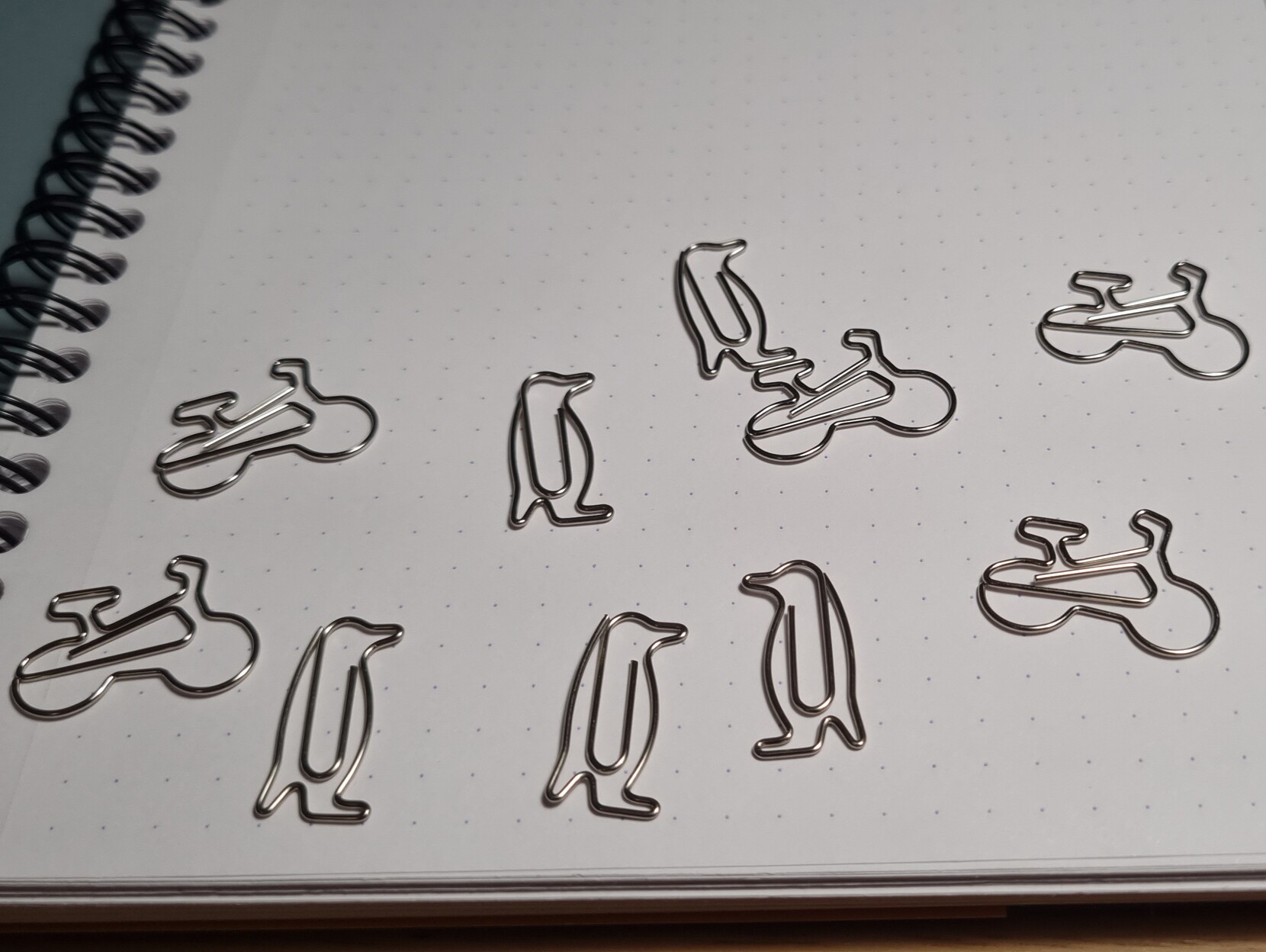 It' ten paperclips on a dot grid notepad. Five are shaped like penguins and five are shaped like bikes.
