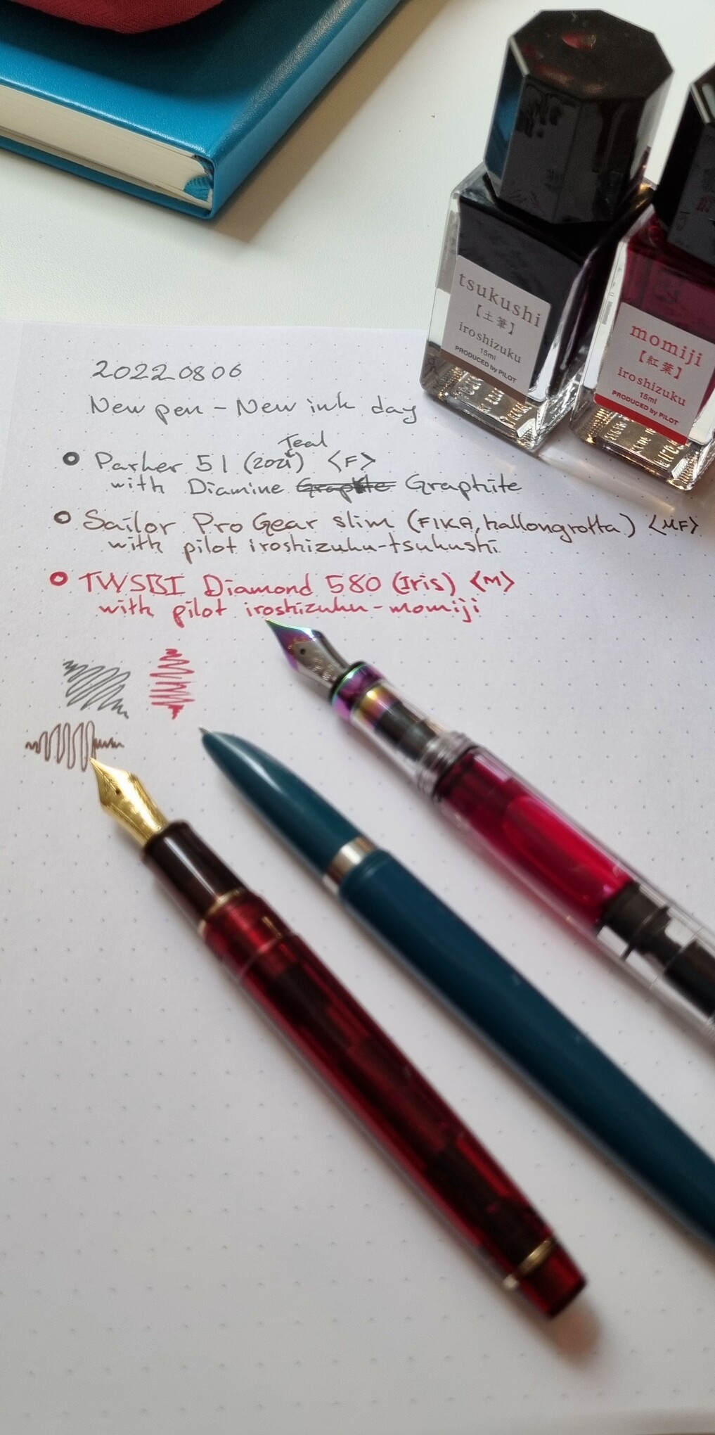 Three pens layed out on a paper with text by the fespective pens
"20220806
New pen - new ink day
○ Parker 51 (2021 Teal) <F>
     with Diamine Graphite
○ Sailor Pro Gear Slim (FIKA, hallongrotta) <MF>
     with Pilot iroshizuku - tsukushi
○ TWSBI Diamond 580 (Iris) <M>
     with Pilot irushizuku - momiji "