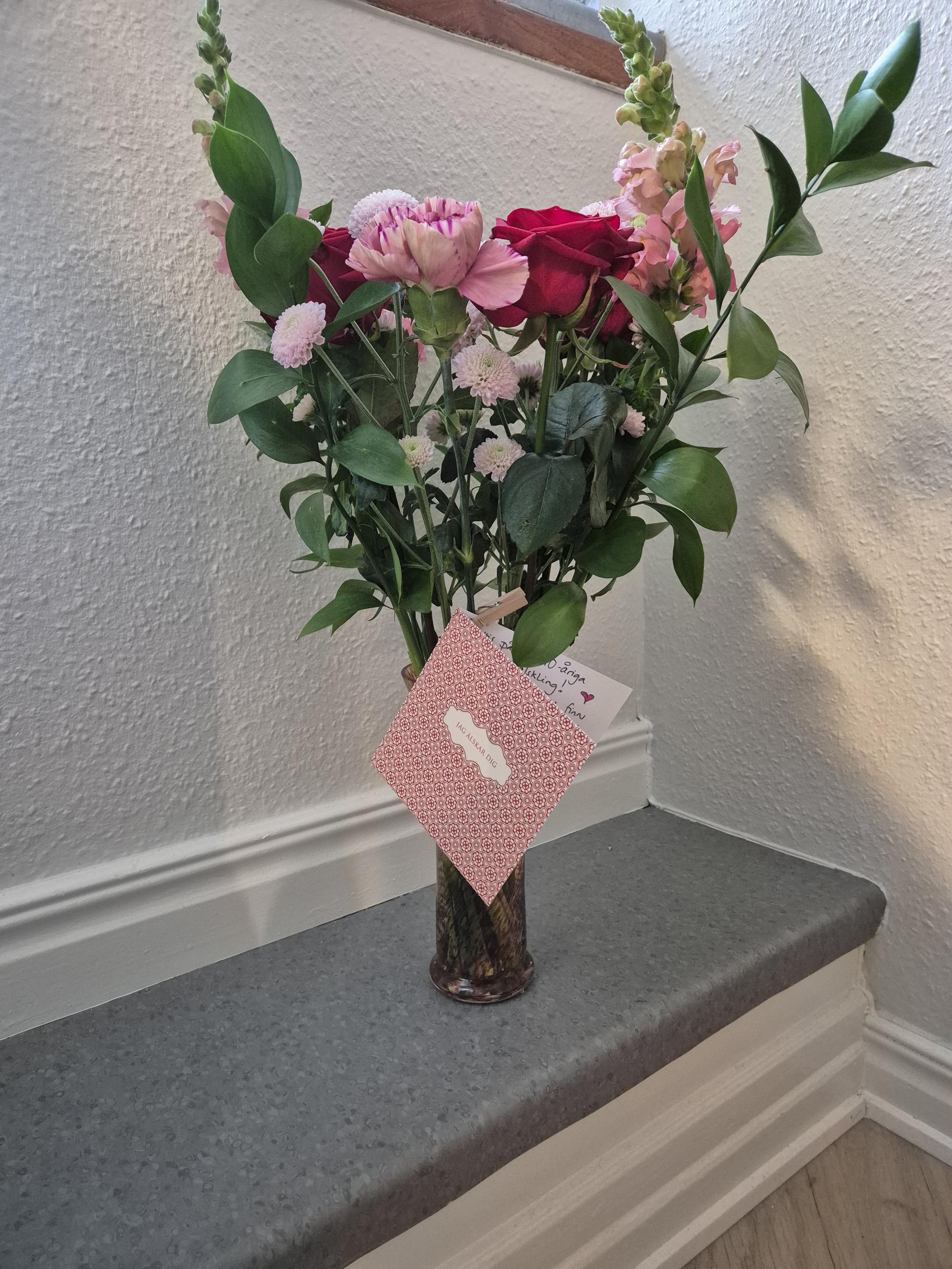 En blombukett i rött och rosa står i en vas mot vit bakgrund.