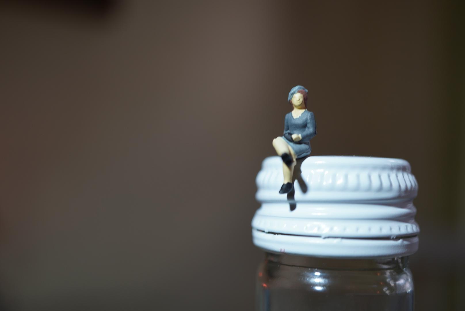 A tiny model of a tiny lady is sitting on the cap of a bottle