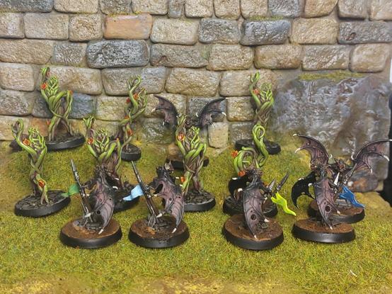 6 bats and 7 triffids posing for glam shots in a patch of grass in front of a city wall