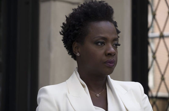 Viola Davis in Widows. She has short hair and wears a styish white suit. She's looking to her left with a sad expression.