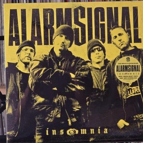Ein Albumcover der Band Alarmsignal, das in einem kräftigen gelb-schwarzen Farbschema gehalten ist. Vier Mitglieder posieren selbstbewusst und tragen dunkle Kleidung und Hüte. Der Albumtitel "insomnia" und der Name der Band sind deutlich zu erkennen.