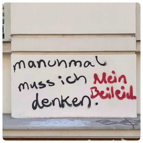 The image features graffiti on a wall, displaying the text "imanchmal muss ich denken. Mein beileid." The words are written in black and red spray paint on a light-colored background.