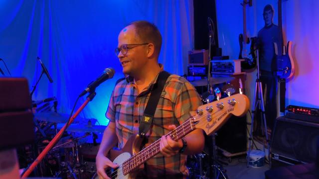 Person holding a bass guitar talking into a microphone