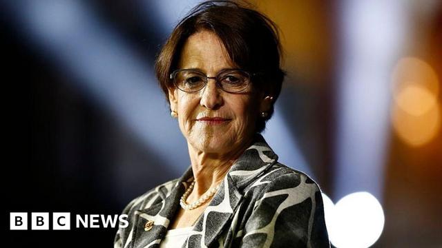 Headshot of Susana Villarán - who has short brown hair - wearing glasses, a pearl necklace and a patterned black and white jacket while on stage giving a speech in 2013 in Lima, Peru.