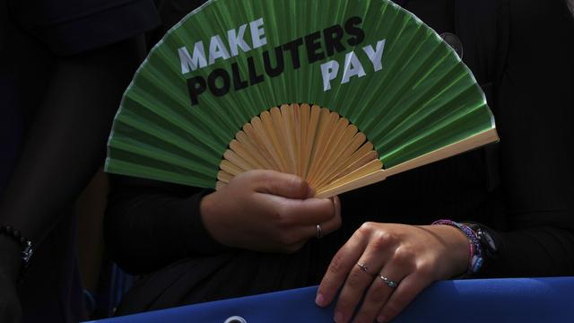 An activist holds a fan that reads "make polluters pay" as they demonstrate outside the International Court of Justice ahead of an advisory opinion on what legal obligations nations have to address climate change and which consequences they may face if they don't, on Wednesday, July 23, 2025, in The Hague, Netherlands. (AP Photo/Peter Dejong)