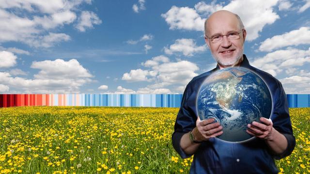 Harald Lesch auf Wiese mit Globus in der Hand.