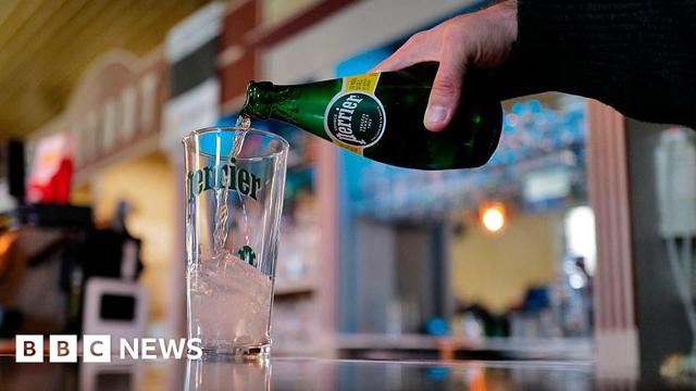 A man pours a bottle of Perrier water into a glass on a bar