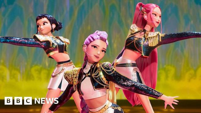 A scene from the animation Kpop Demon Hunters, where three young women - K-pop idols - are dressed in shiny costumes and performing on a stage. They are posing with their arms outstretched.