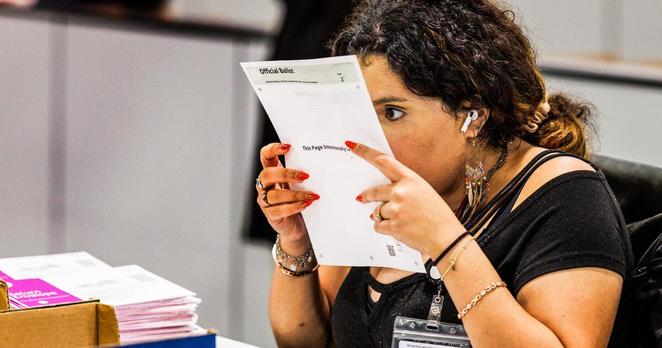 An election worker inspects a Vote by Mail ballot