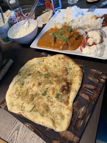 Hvitløknan liggende ved siden av tallerken med lam tikka masala, ris, mango chutney, raita dip på tomat og rødløk. Toppen drysset med koriander.