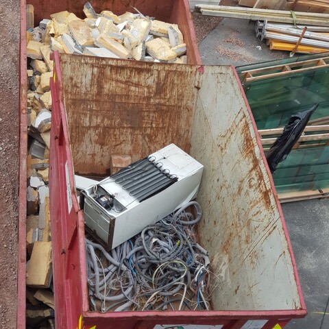 A photograph of a fridge or freezer with other scrap in a rusty container on a construction site.