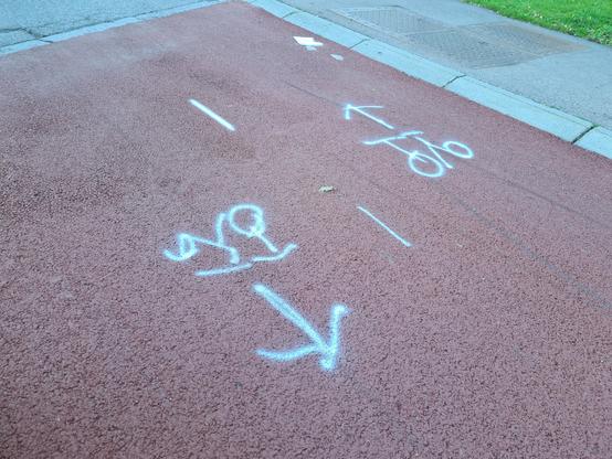 Midlertidige symboler malt med spraymaling på rød asfalt. Symbolene er sykler, men de er bare tegnet som to hjul med noen tilfeldige streker mellom.