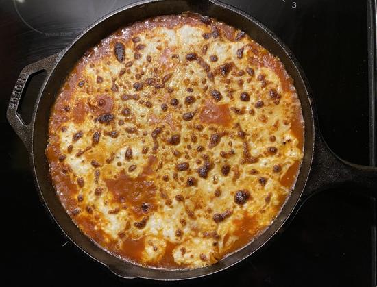 Cast iron skillet filled with lasagna. The cheese on top is browned in places