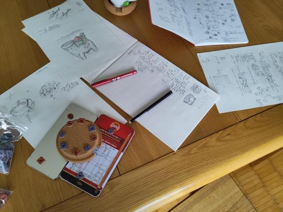 Table with a bunch of sketches and notes. Some board game tokens used to prototype a puzzle lock.