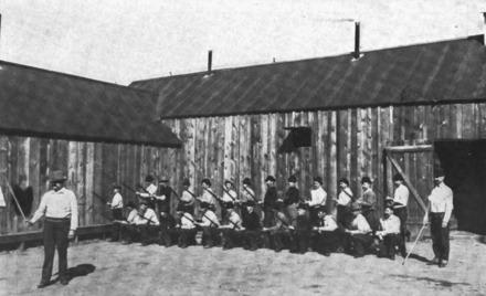 Prisoners drill with wooden rifles in the "bullpen," Wardner, Idaho, 1899. By uncredited - T. A. Rickard, The Bunker Hill Enterprise (San Francisco: Mining &amp; Scientific Press, 1921) 137., Public Domain, https://commons.wikimedia.org/w/index.php?curid=55853856