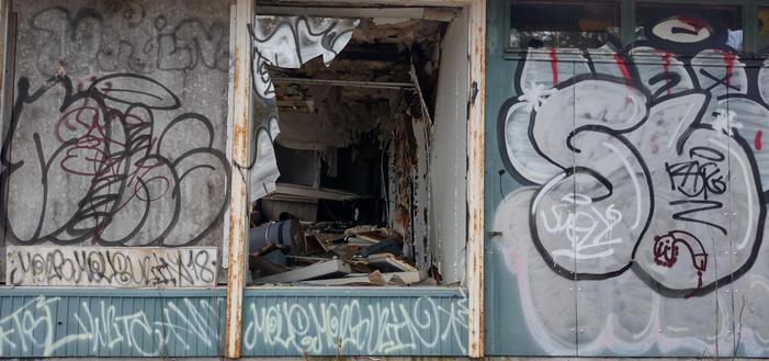 Broken window at an abandoned gas station, closed for decades, now utterly trashed and tagged.