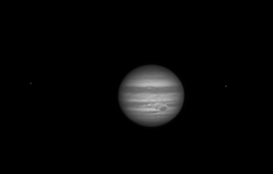 The planet Jupiter showing its clouds, bands and the Great Red Spot. Orbiting around it Europa and Io. Mono image.