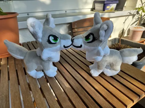 Two grey wolf plushies placed in front of each other with the noses touching.