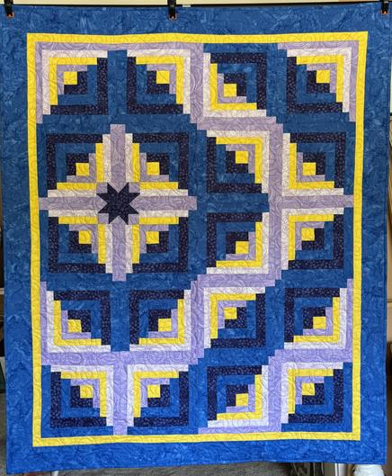 Front of a quilt that has blues, purples, and yellow in a log cabin pattern.