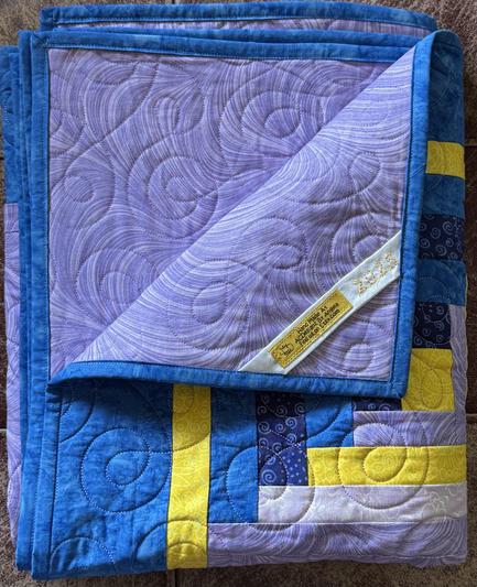 Folded quilt with a corner of it turned back exposing a label going diagonally from corner to corner.
